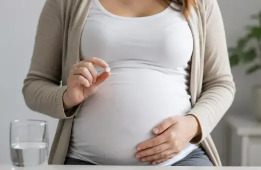 Kobieta w ciąży trzyma tabletkę, zastanawiając się nad aspiryną w ciąży. Obok stoi szklanka wody.