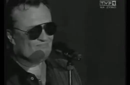 Mężczyzna w okularach przeciwsłonecznych śpiewa do mikrofonu. Widać logo TVP1. A po nocy przychodzi dzień.