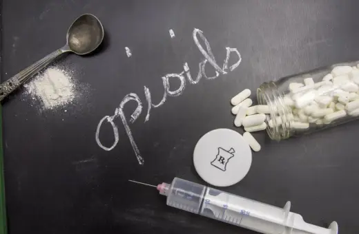 Napis "opiaty" na tablicy, obok łyżki z proszkiem, strzykawki i butelki z tabletkami.