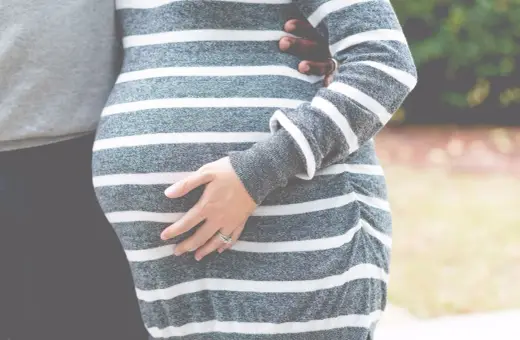 Dłoń kobiety obejmuje ciążowy brzuszek w paski. To piękny widok, choć czasem ciąża wiąże się z wyzwaniami, jak krwiak w ciąży.