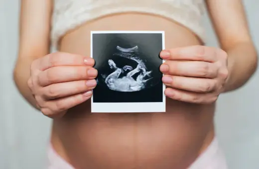 Ciężarna kobieta trzyma zdjęcie USG, na którym widać dziecko. Widać też łożysko na przedniej ścianie.