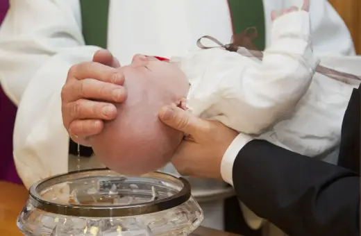 Chrzest chłopca: biała szatka, szklana chrzcielnica i woda święcona.