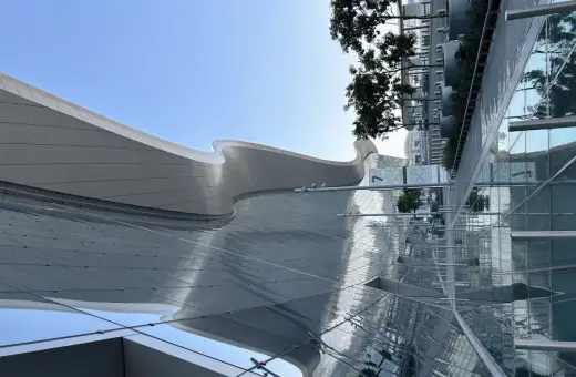 Nowoczesna architektura AUH Zayed International z falującym dachem i szklanymi fasadami odbijającymi niebo i zieleń.