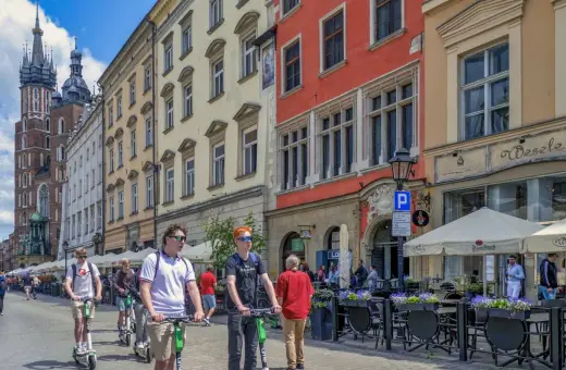 Młodzi ludzie na hulajnogach w Krakowie, idealne na city break. W tle Sukiennice i Kościół Mariacki.