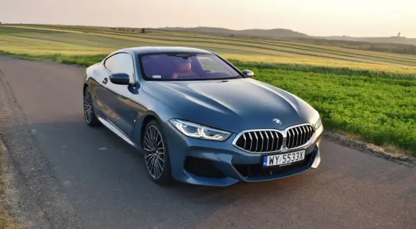 Niebieskie BMW 840d na tle pól zbożowych o zachodzie słońca.