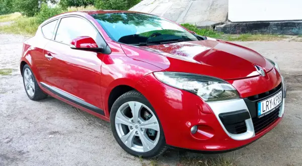 Czerwone Renault Megane Coupe 3 na tle betonowej konstrukcji i zieleni.