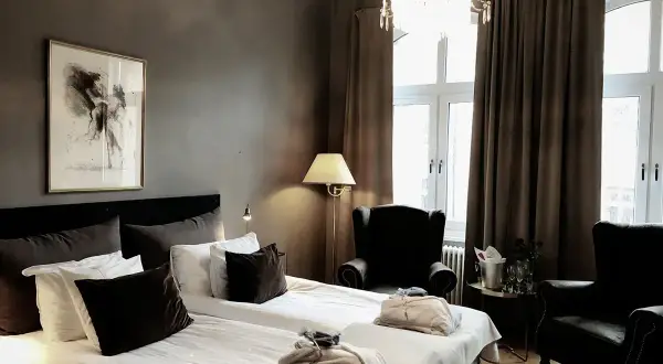 Ett elegant hotellrum inredning med dubbelsäng, bekväma fåtöljer, en kristallkrona och konst på väggen.