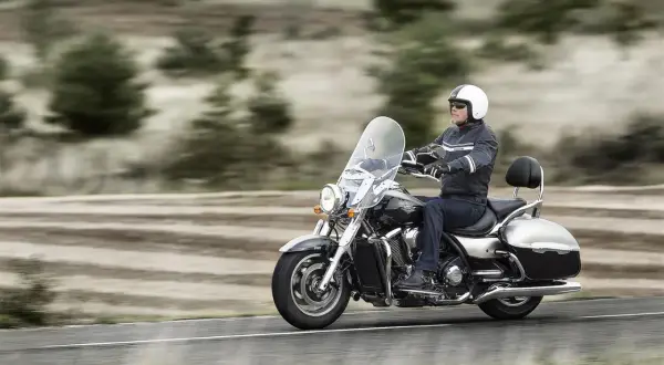 Mężczyzna w kasku jedzie na lśniącym motorze chopper, przemierzając pustą drogę wśród drzew.