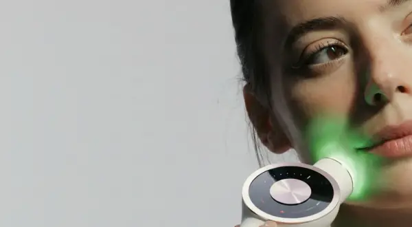 Une femme utilise un appareil de luminothérapie LED pour le visage, projetant une lumière verte apaisante.