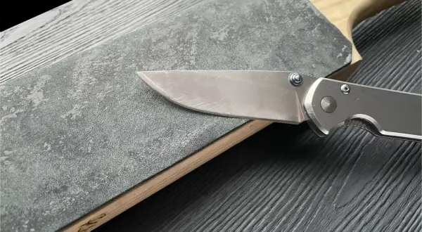En kniv slipas mot en grov slipsten med trähandtag.