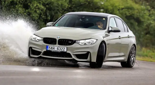 Szary BMW F80 M3 pokonuje kałużę, tworząc efektowny rozbryzg wody.
