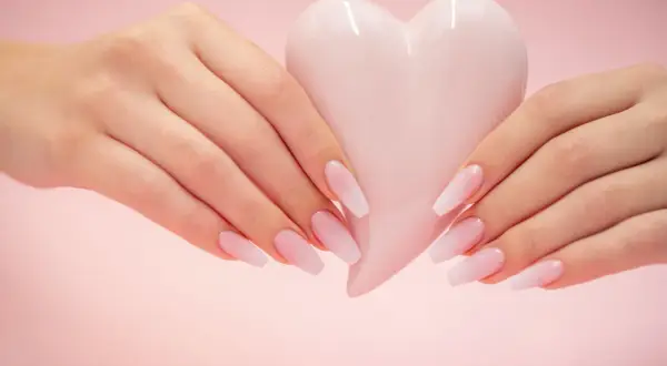 Mains délicates tenant un cœur rose pâle, manucure baby boomer couleur pastel.