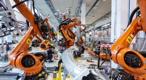 Pomarańczowe ramiona robotów KUKA pracują w fabryce, tworząc przyszłość. To zaawansowana robota automatyka.