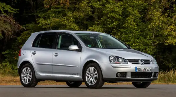 Srebrny Volkswagen Golf 5 z 2004 roku zaparkowany na drodze, z zielonym lasem w tle.