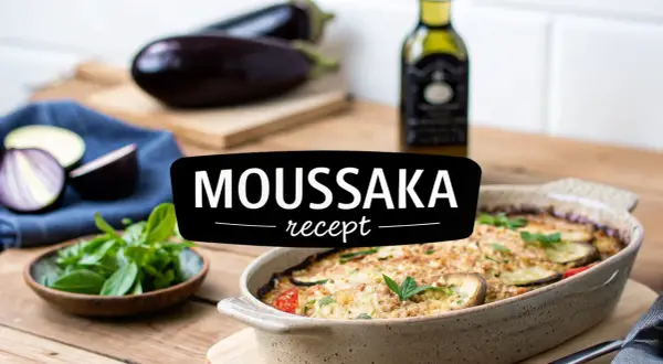 En ugnsbakad moussaka i en keramikform, med aubergine, tomater och örter. Texten "MOUSSAKA recept" syns tydligt.