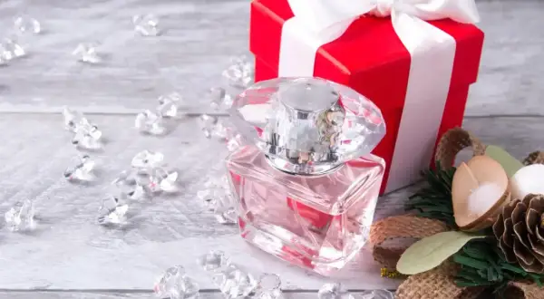 Eleganckie perfumy w szklanej butelce, czerwone pudełko z kokardą i ozdoby. Idealny pomysł, jak zapakować perfumy na prezent.