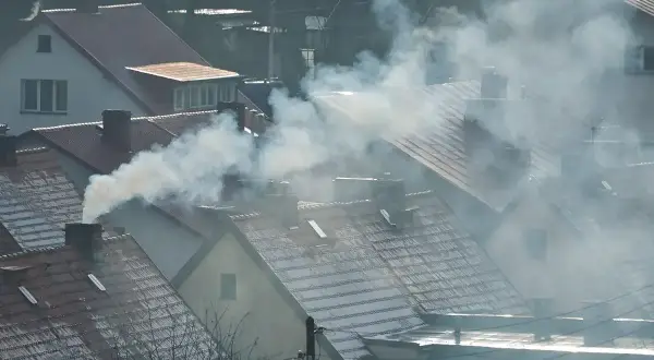 Dym wydobywający się z kominów domów na tle zachmurzonego nieba.