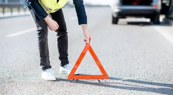 Hombre con chaleco reflectante coloca un triángulo de señalización tras una detención de coche en la carretera.