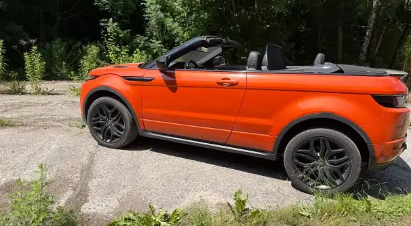 Orange Range Rover Evoque Cabrio, offen, steht auf einem Schotterweg. Mögliche Probleme mit dem Verdeck?