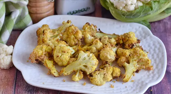 Cavolfiore dorato e croccante, cotto in friggitrice ad aria, servito su un piatto bianco.