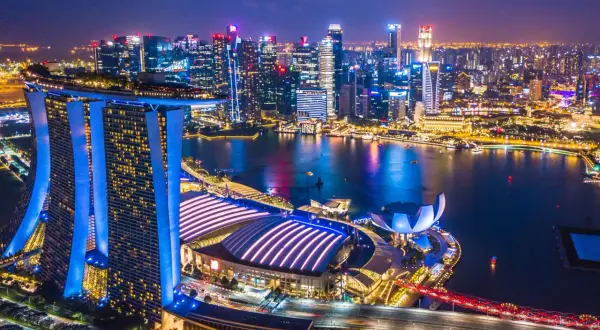 Nocny widok na Singapur z oświetlonymi drapaczami chmur i Marina Bay Sands. Miasto tętni życiem, a jego rozwój, jak singapur szczepienia, świadczy o postępie.
