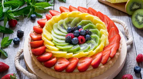 Crostata di frutta con decorazioni colorate di fragole, kiwi, ananas e frutti di bosco.