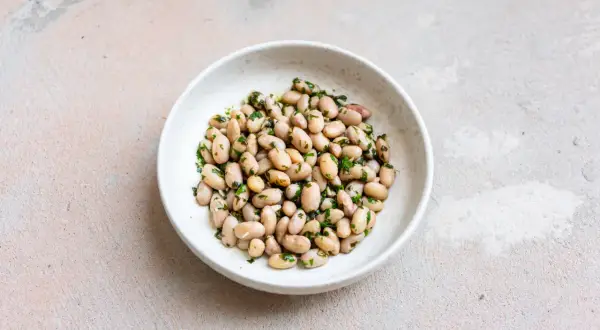 Eine Schüssel mit gekochten, hellen Bohnen, verfeinert mit gehackter Petersilie. Diese Fagioli Borlotti sind ein köstlicher deutscher Klassiker.