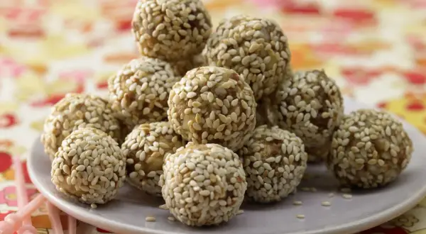 Ein Haufen köstlicher Energy Balls, umhüllt von Sesam, auf einem Teller. Perfekt für einen schnellen Energieschub!