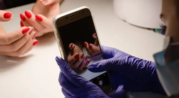 Ręce w fioletowych rękawiczkach robią zdjęcie pięknych, czerwonych paznokci na telefonie. Oto jak zrobic ladne zdjecia paznokci.