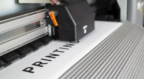 Drukarka wielkoformatowa drukuje napis "PRINTING" na białym papierze.