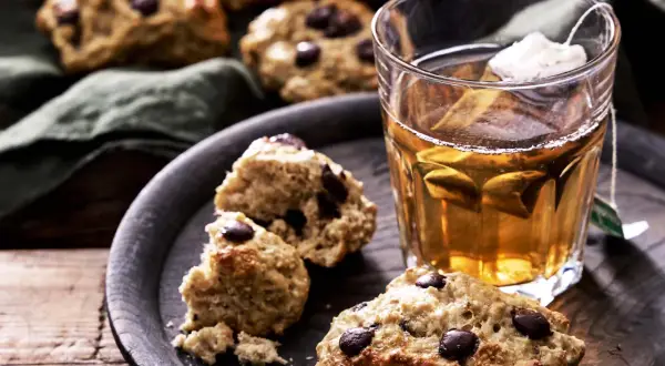 Nyttigare scones med chokladbitar på en mörk bricka bredvid ett glas te. Perfekt fika!