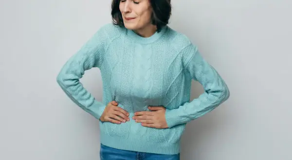 Kvinna med händerna på magen, ansiktet förvridet av smärta. Ett tydligt tecken på stressmage symptom.