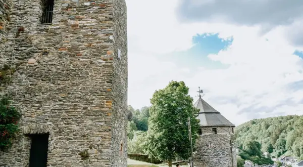 Ein Mann spaziert auf einem Weg zur Burg Monschau, vorbei an alten Steintürmen und grünen Hügeln.