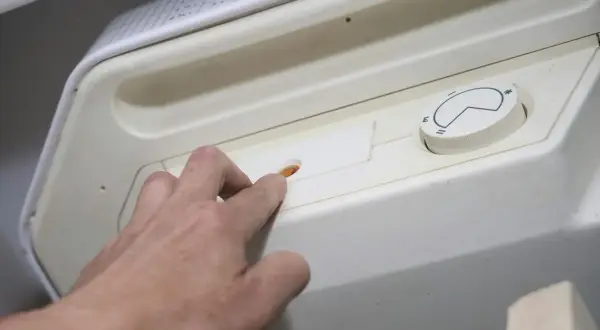 Dłoń naciska pomarańczowy przycisk, inicjując pierwsze uruchomienie pieca gazowego. Obok pokrętło regulacji temperatury.
