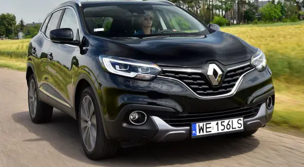 Czarny Renault Kadjar w ruchu. Kierowca w okularach przeciwsłonecznych. Wiele pozytywnych renault kadjar opinie potwierdza jego walory.