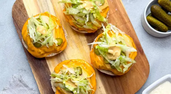 Vier offene **Big Mac Rollen** mit Käse, Salat, Gurken und Sauce auf einem Holzbrett.