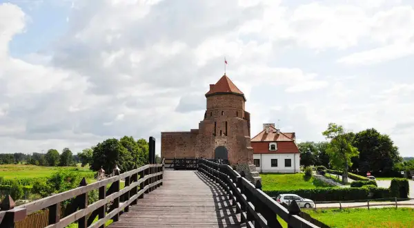 Drewniany most prowadzi do ceglanego zamku z czerwoną wieżą. Idealne miejsce na weekendowe wypady, to jedne z fajnych miejsc niedaleko Warszawy na weekend.