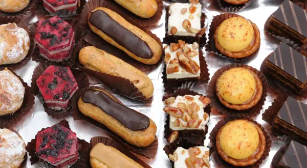 Variedad de petit fours: éclairs de chocolate y caramelo, pastelitos de frutas rojas, cuadrados de crema con nueces, tartas de crema amarilla y pastelitos de chocolate.