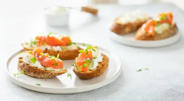 Bruschetta saumon : toasts grillés garnis de fromage frais, fines tranches de concombre, saumon fumé et herbes fraîches.