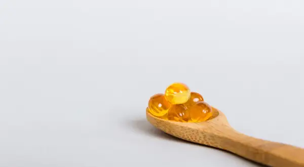 Houten lepel met gele capsules, mogelijk ter bestrijding van vitamine d tekort duizeligheid.