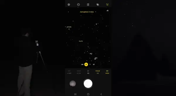 Mężczyzna robi zdjęcie nocnego nieba z Saturnem i Plutonem za pomocą telefonu Samsung. Tryb Astrophoto ustawiony na 4 minuty.