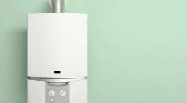 Chaudière basse température blanche, moderne, avec un conduit métallique, installée sur un mur vert pâle.