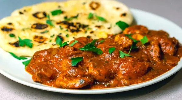 En krämig chicken tikka masala med bitar av kyckling i en smakrik tomatsås, serverad med fluffigt naanbröd.