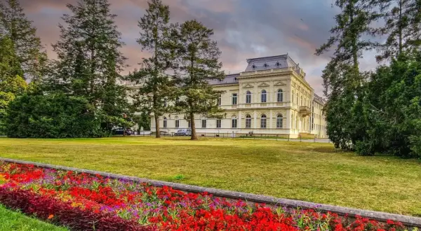 Piękny budynek sanatorium otoczony drzewami i kolorowymi kwiatami. Dowiedz się o nowe zasady wyjazdu do sanatorium na NFZ.