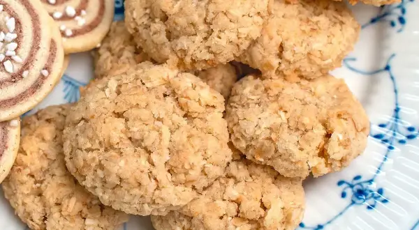 En hög med hembakade havrekakor, perfekta för ett enkelt havrekakor recept. Bredvid syns några rullade kakor med pärlsocker.