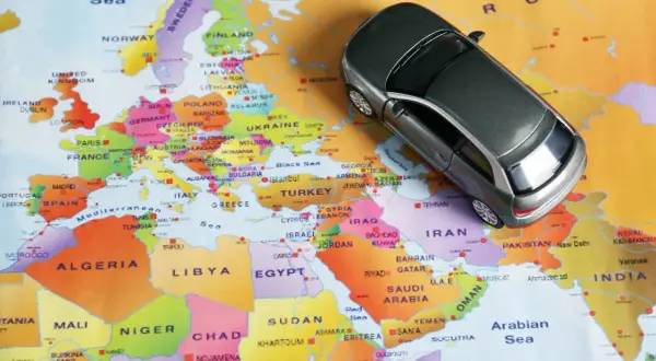 Une petite voiture grise sur une carte d'Europe. Conduite à gauche quel pays ? L'image suggère un voyage en Europe, où la conduite à gauche est la norme dans de nombreux pays.
