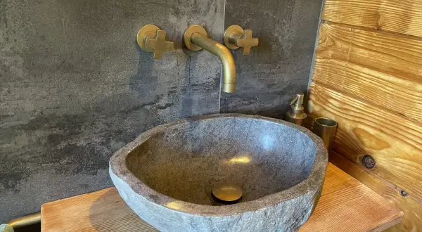 Lavabo in pietra grezza, rubinetteria in ottone e rivestimento in legno: perfette idee bagno montagna per un'atmosfera rustica e accogliente.
