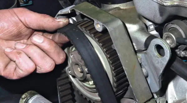 Dłoń mechanika sprawdza stan paska rozrządu, który jest kluczowym elementem silnika.