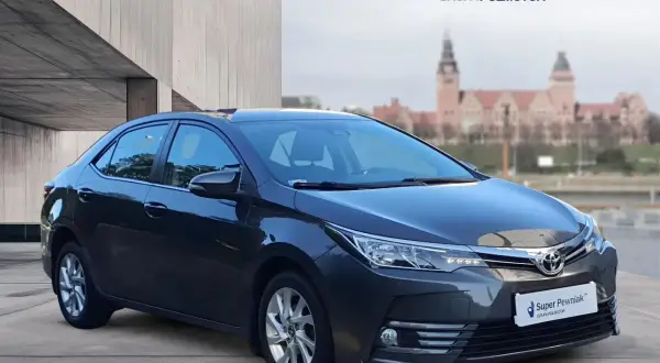 Szary sedan Toyota Corolla używane z salonu, z logo "Super Pewniak" na tablicy rejestracyjnej.