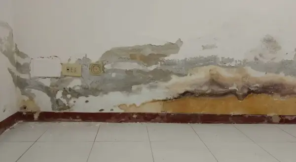 Muri con intonaco antiumido scrostato e macchie di umidità, prese elettriche visibili.